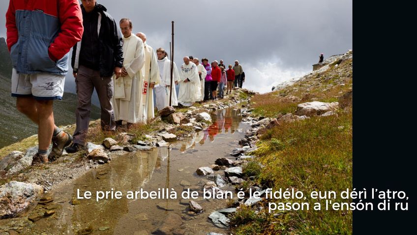 Les curés habillés en blanc et les fidèles, l’un derrière l’autre, passent près du ruisseau 